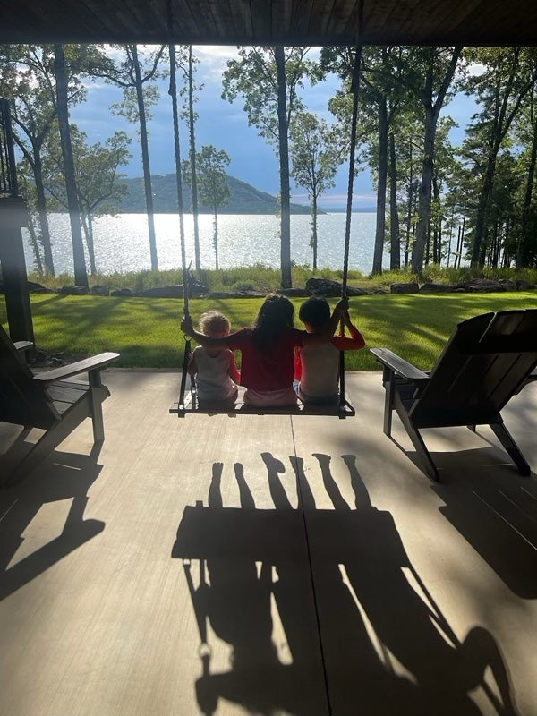 Three children on a swing overlooking a lake with trees and mountains in the background.