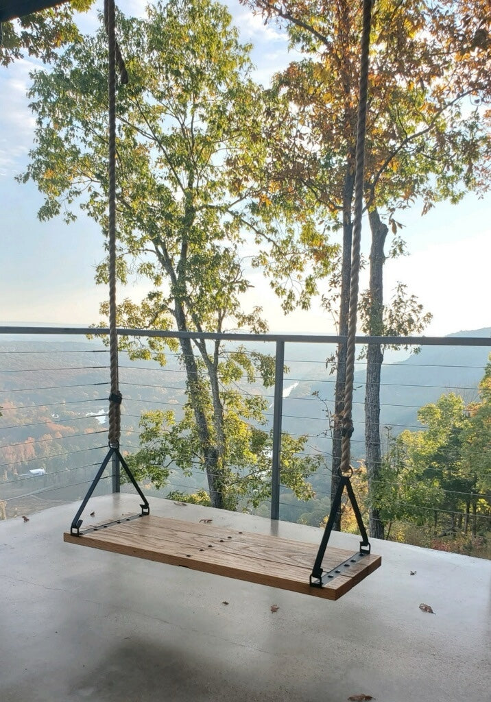 Wooden swing hanging from a tree on a balcony with a scenic view of trees and mountains.