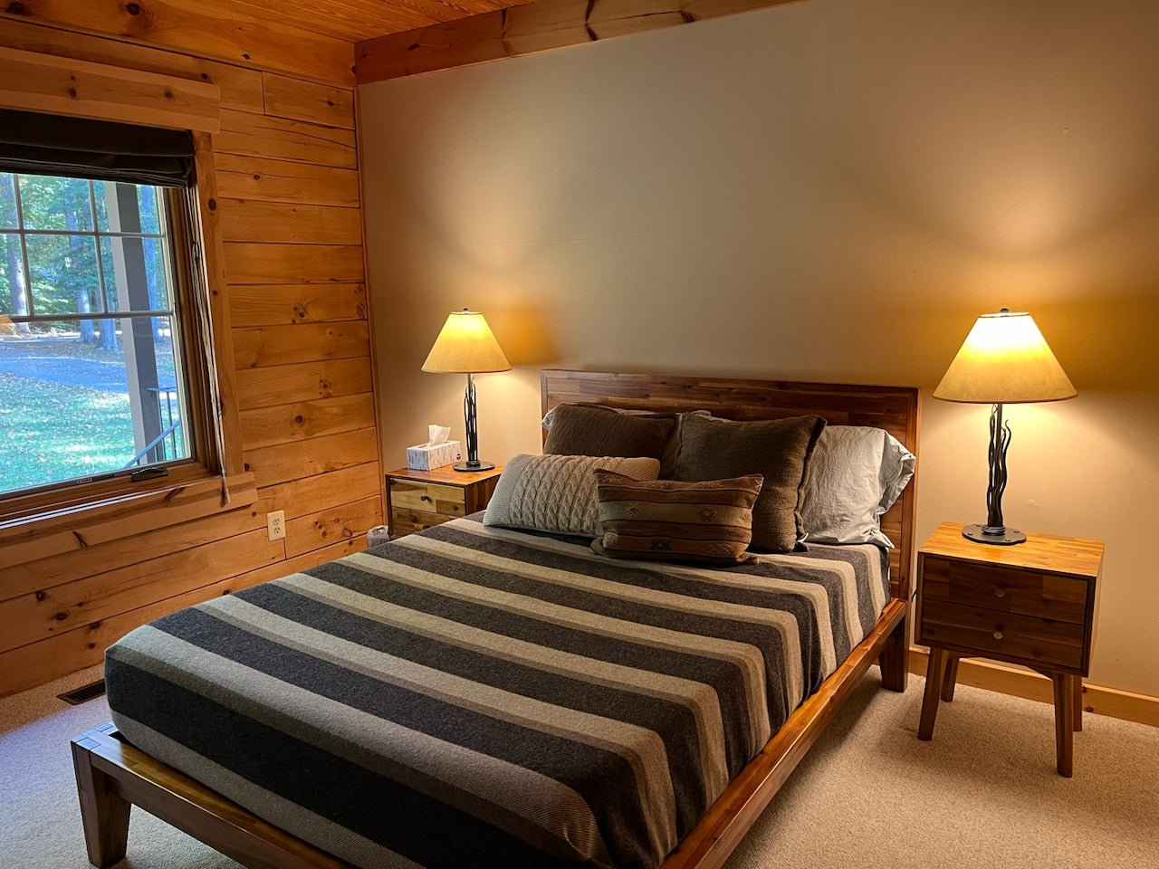 Bedroom with wooden walls, a bed with striped bedding, and two lamps on nightstands.