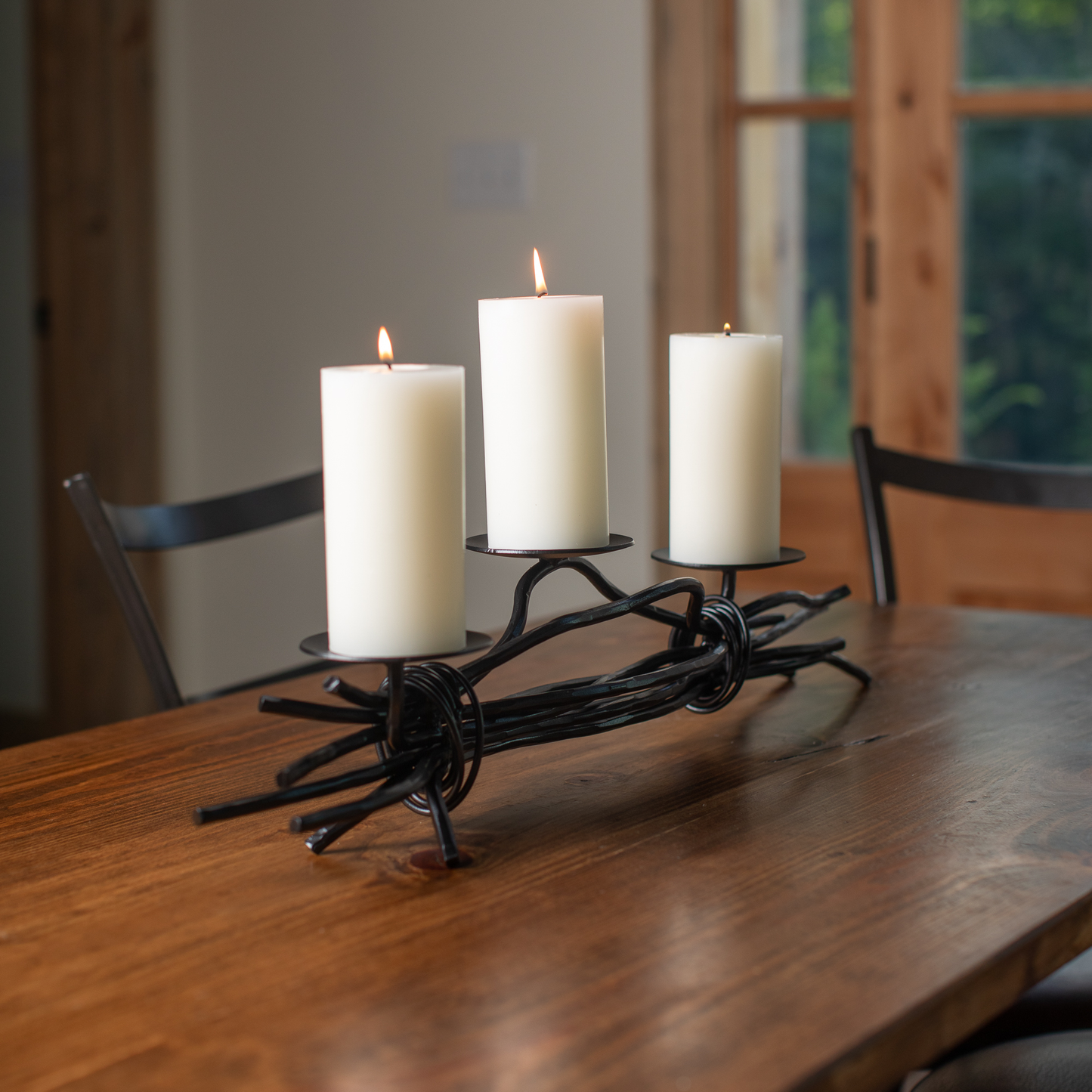 The Urban Forge Black River triple candle holder in a black finish. The candle holder has three white candles and is resting on a dining table.