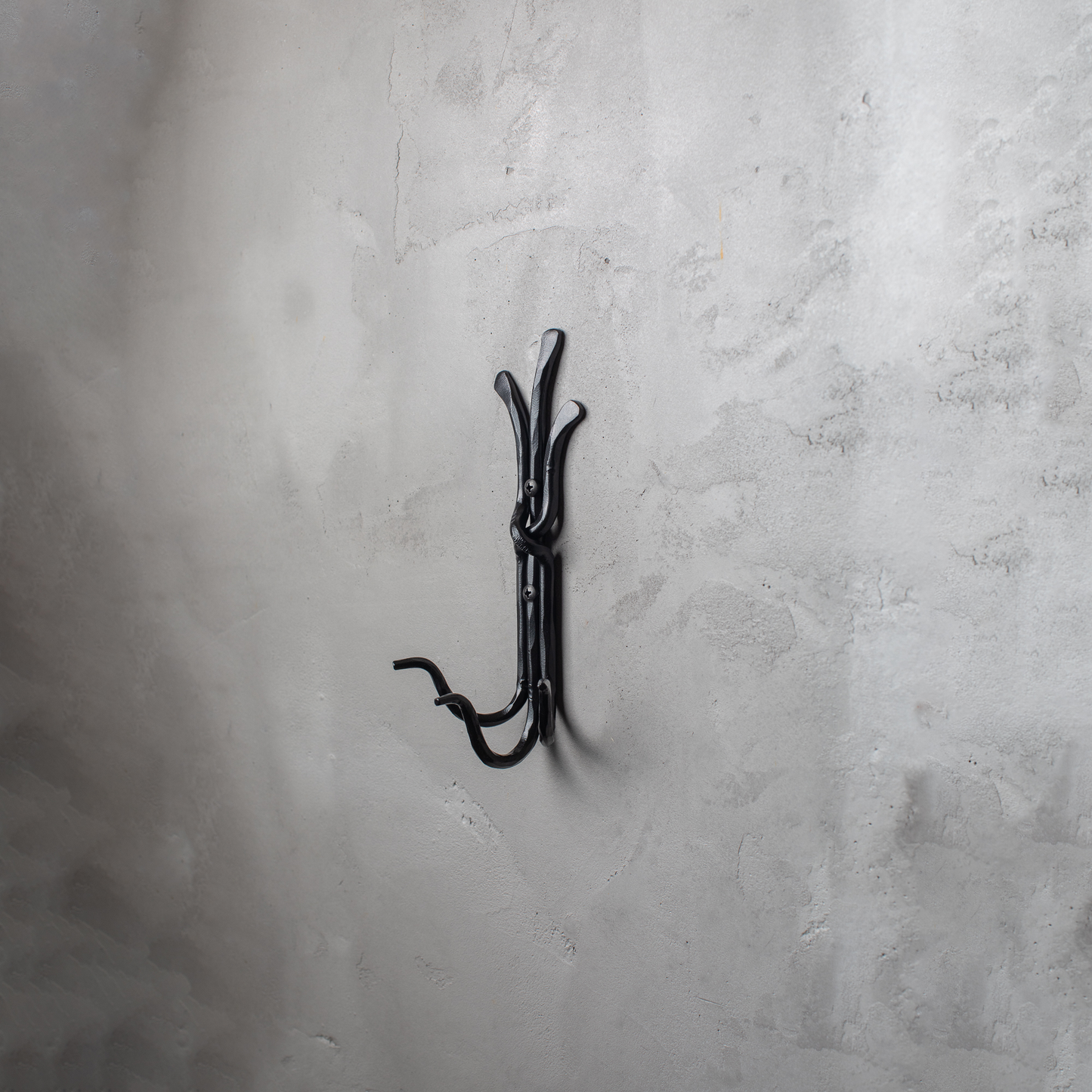 An Urban Forge Black River hand-forged iron triple hook in a black finish. The hook is mounted on a gray wall.