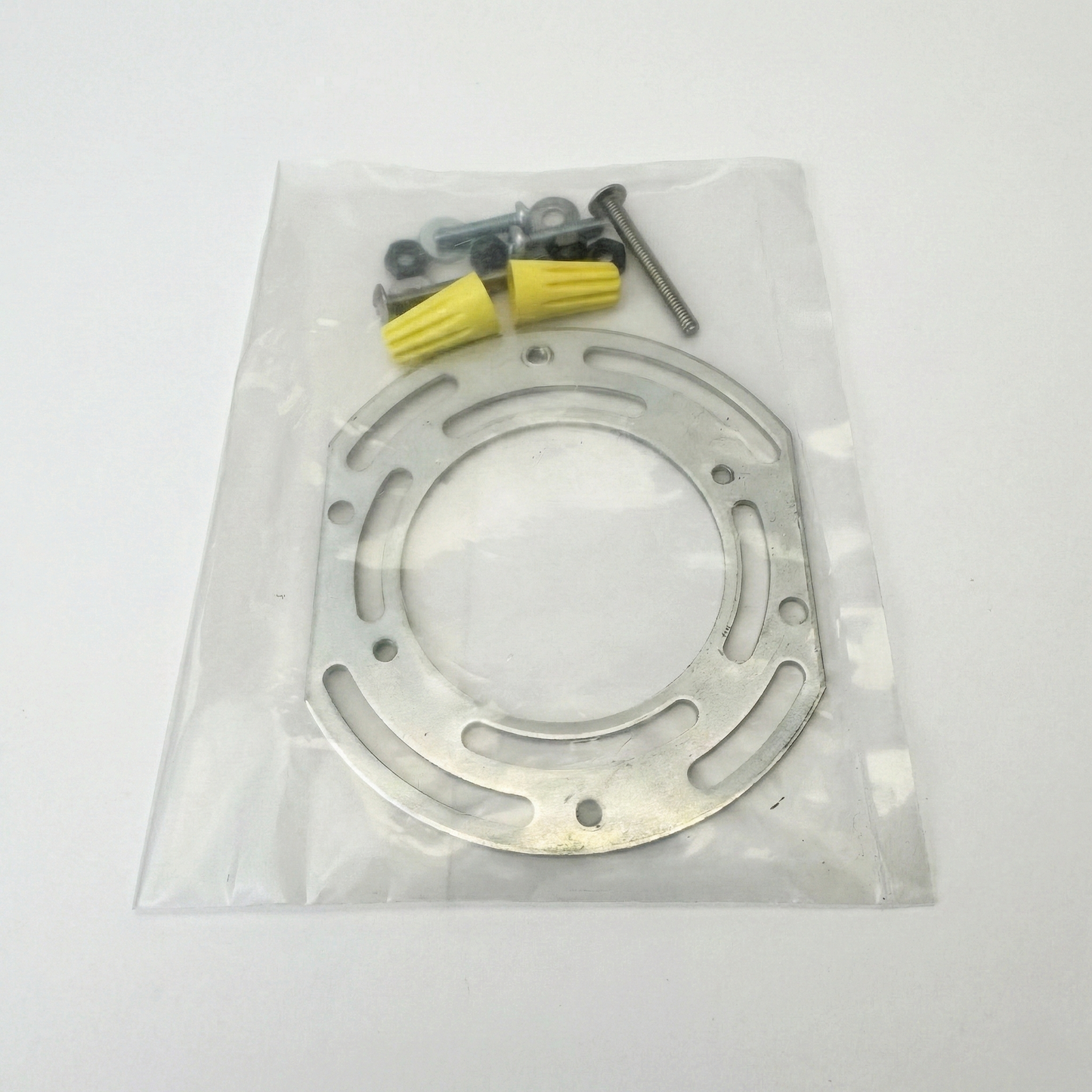 Metallic disc with screws and washers on a clear plastic bag against a white background