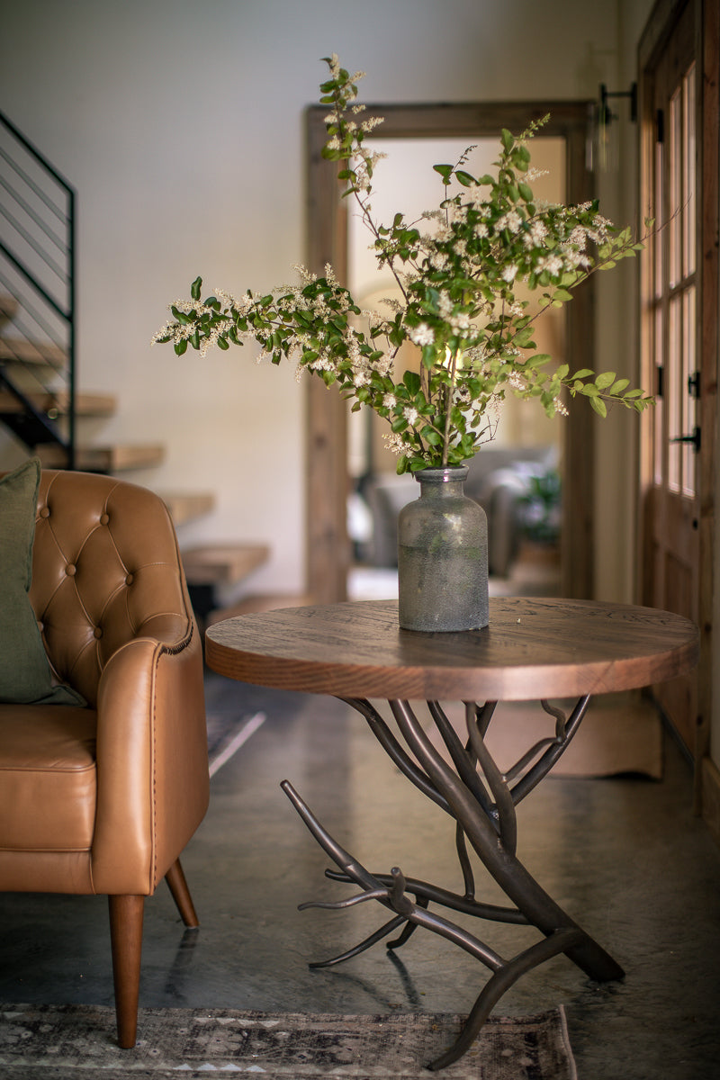 The Urban Forge Driftwood side table rests alongside a comfortable chair in a cozy living room.