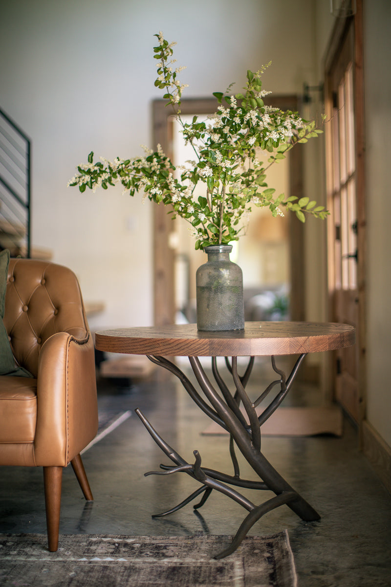 The Urban Forge Driftwood side table rests alongside a comfortable chair in a cozy living room.