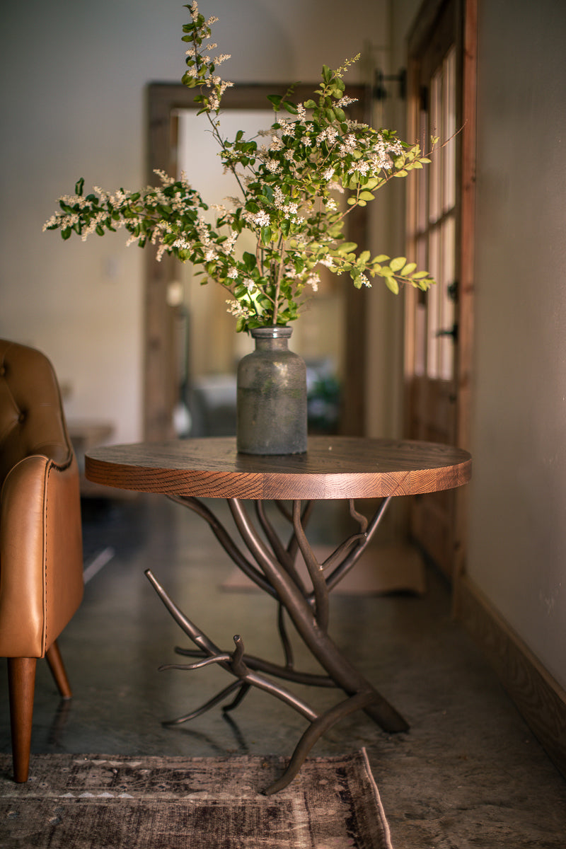 The Urban Forge Driftwood side table rests alongside a comfortable chair in a cozy living room.