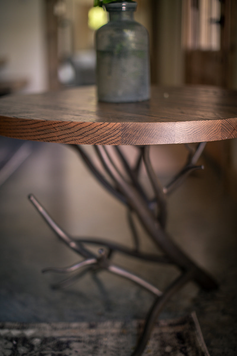 The Urban Forge Driftwood side table rests alongside a comfortable chair in a cozy living room.