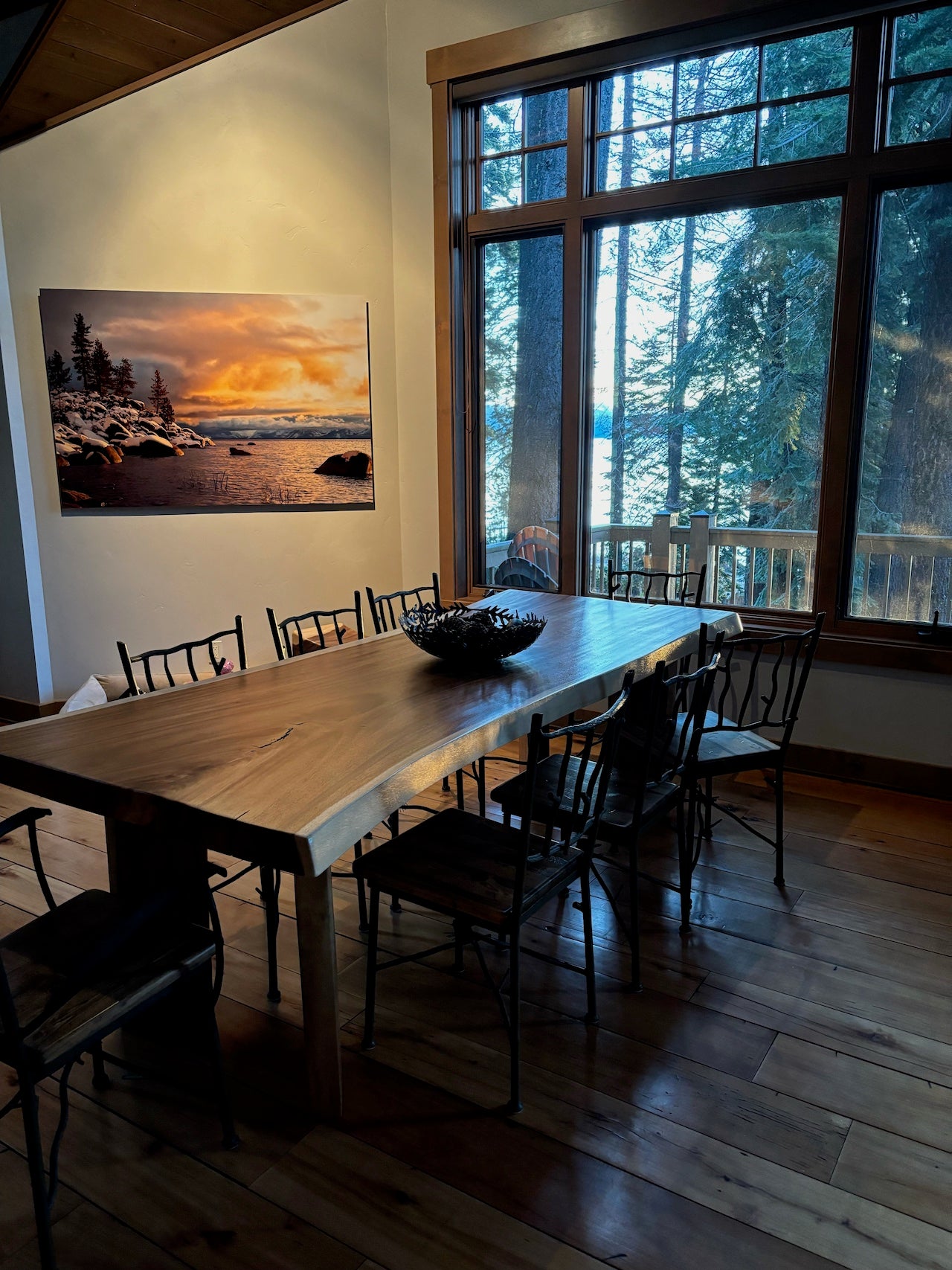 Dining area with wooden table and chairs, large window view of trees, and wall art.