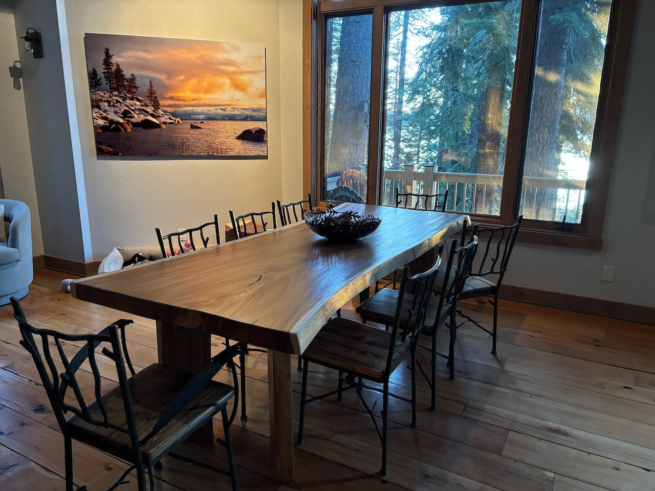 Dining area with a long wooden table and chairs, featuring a large window view of trees.