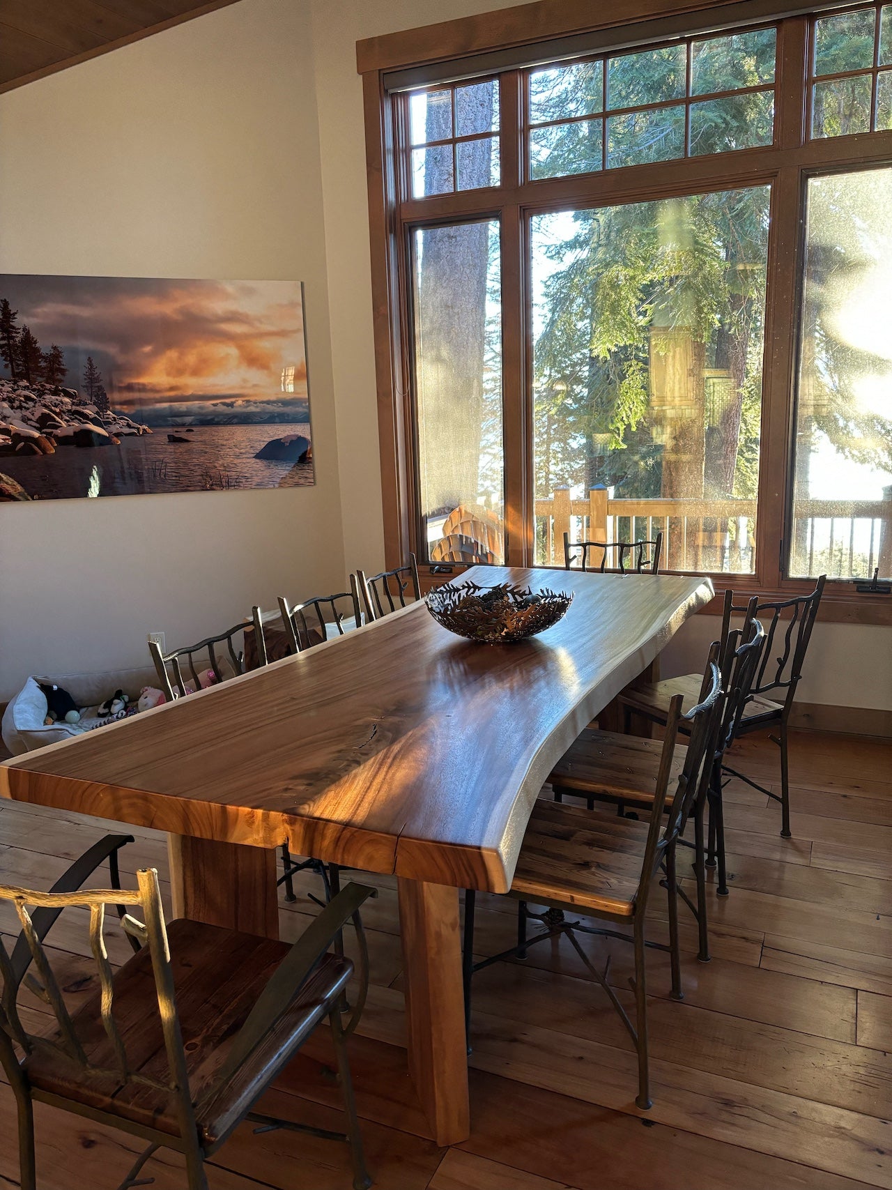 Dining area with a large wooden table and chairs, featuring a scenic painting on the wall.