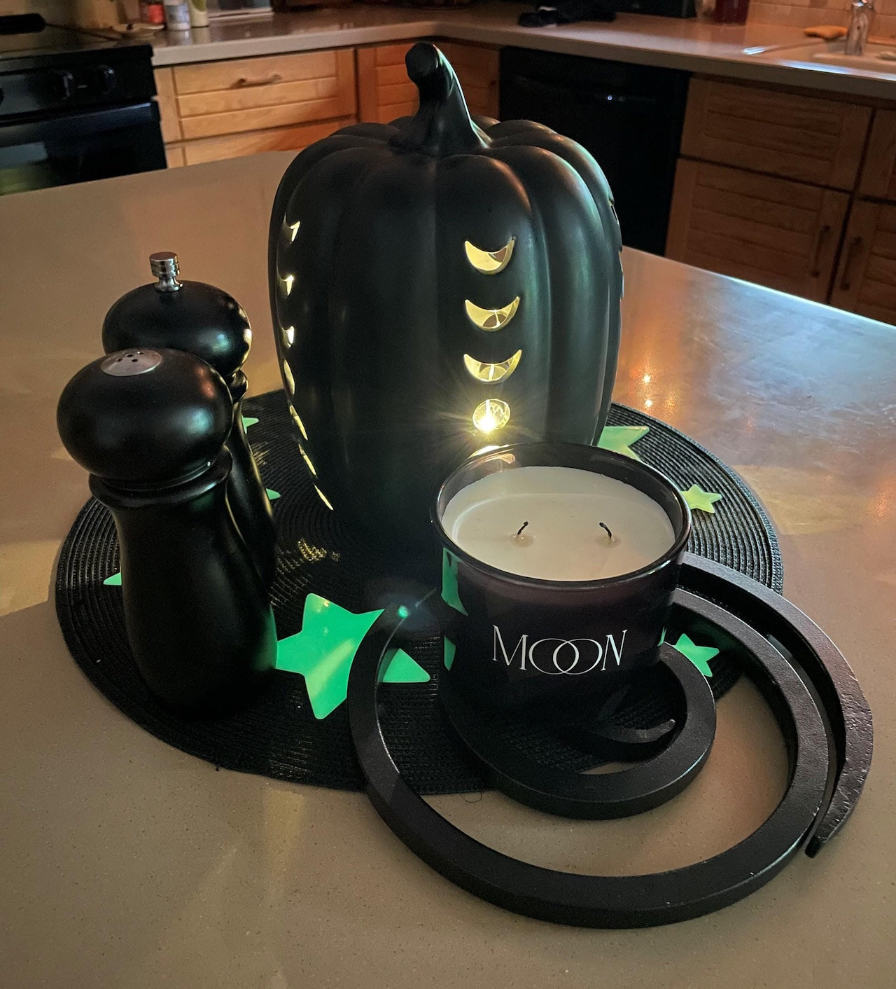Decorative black pumpkin with lit candle and an iron trivet on a kitchen counter