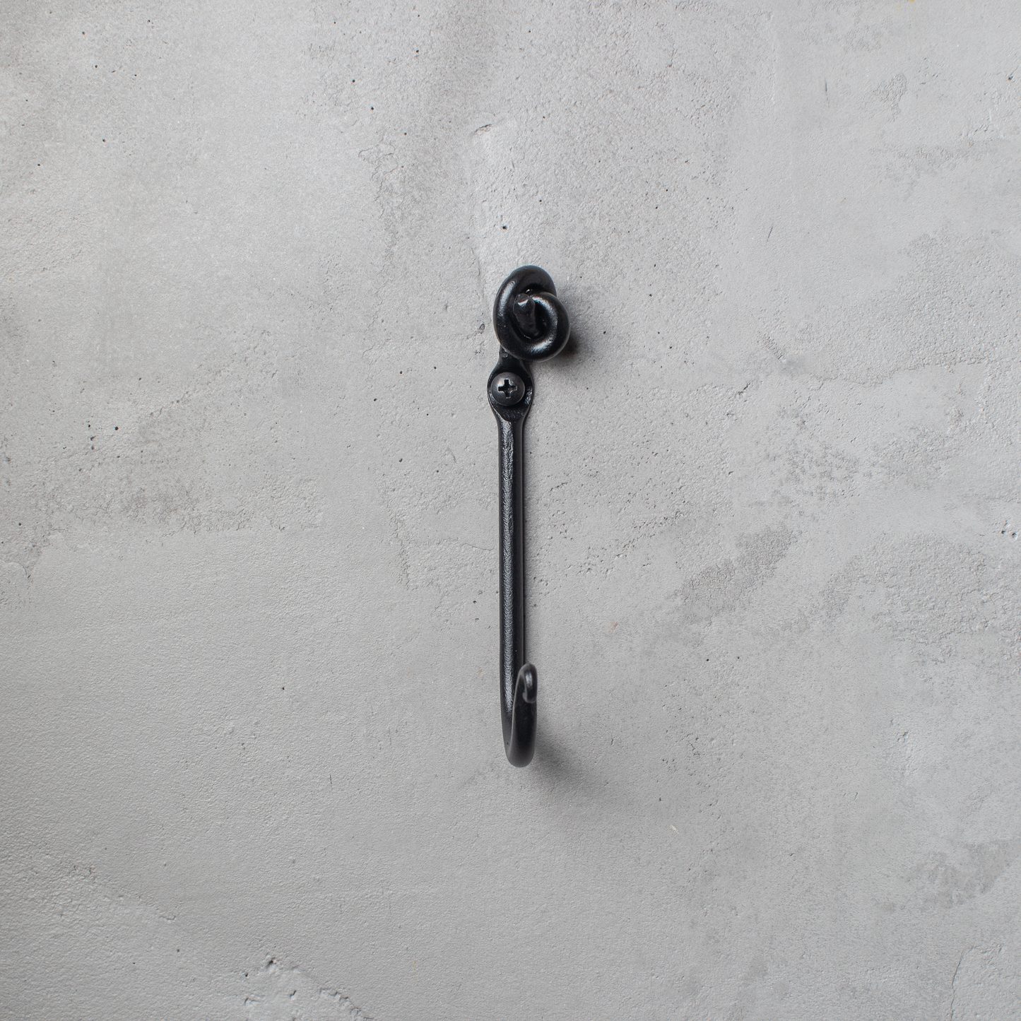 An Urban Forge Knot hand-forged iron single hook in a black finish. The hook is mounted on a gray wall.