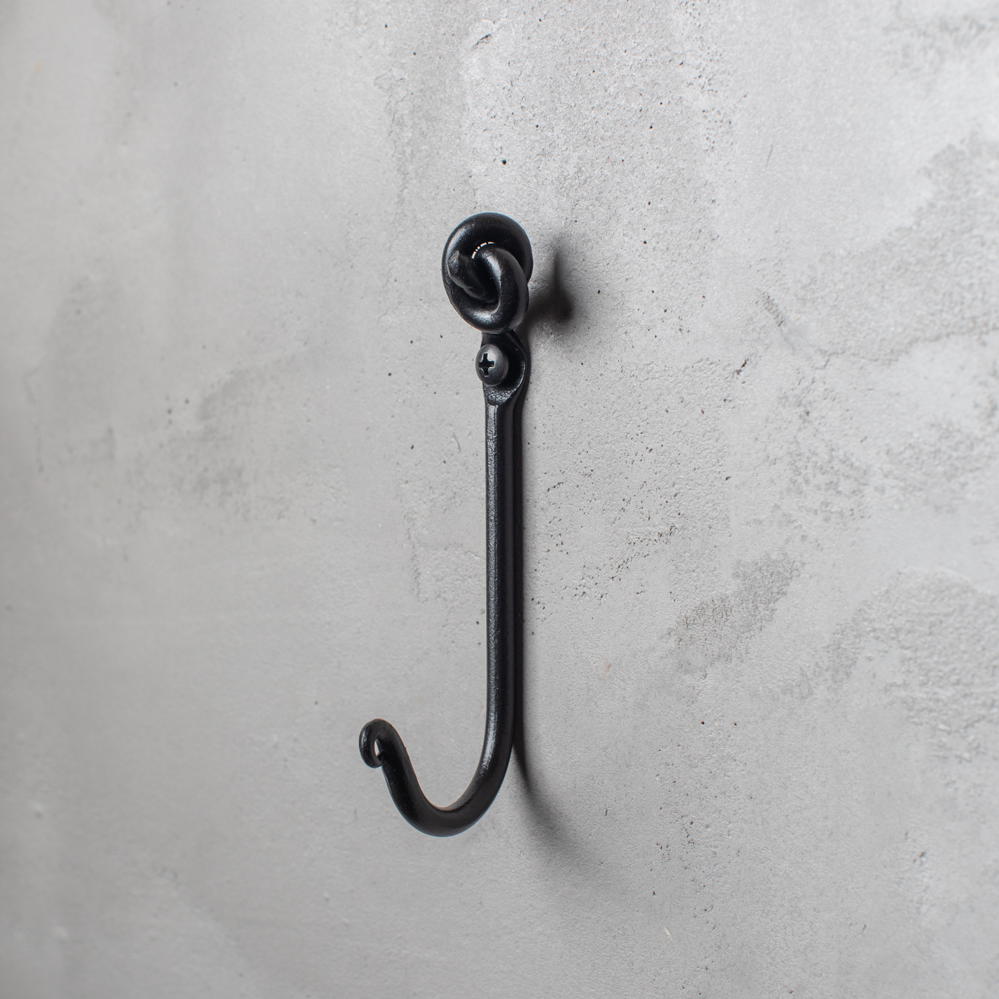 An Urban Forge Knot hand-forged iron single hook in a black finish. The hook is mounted on a gray wall.