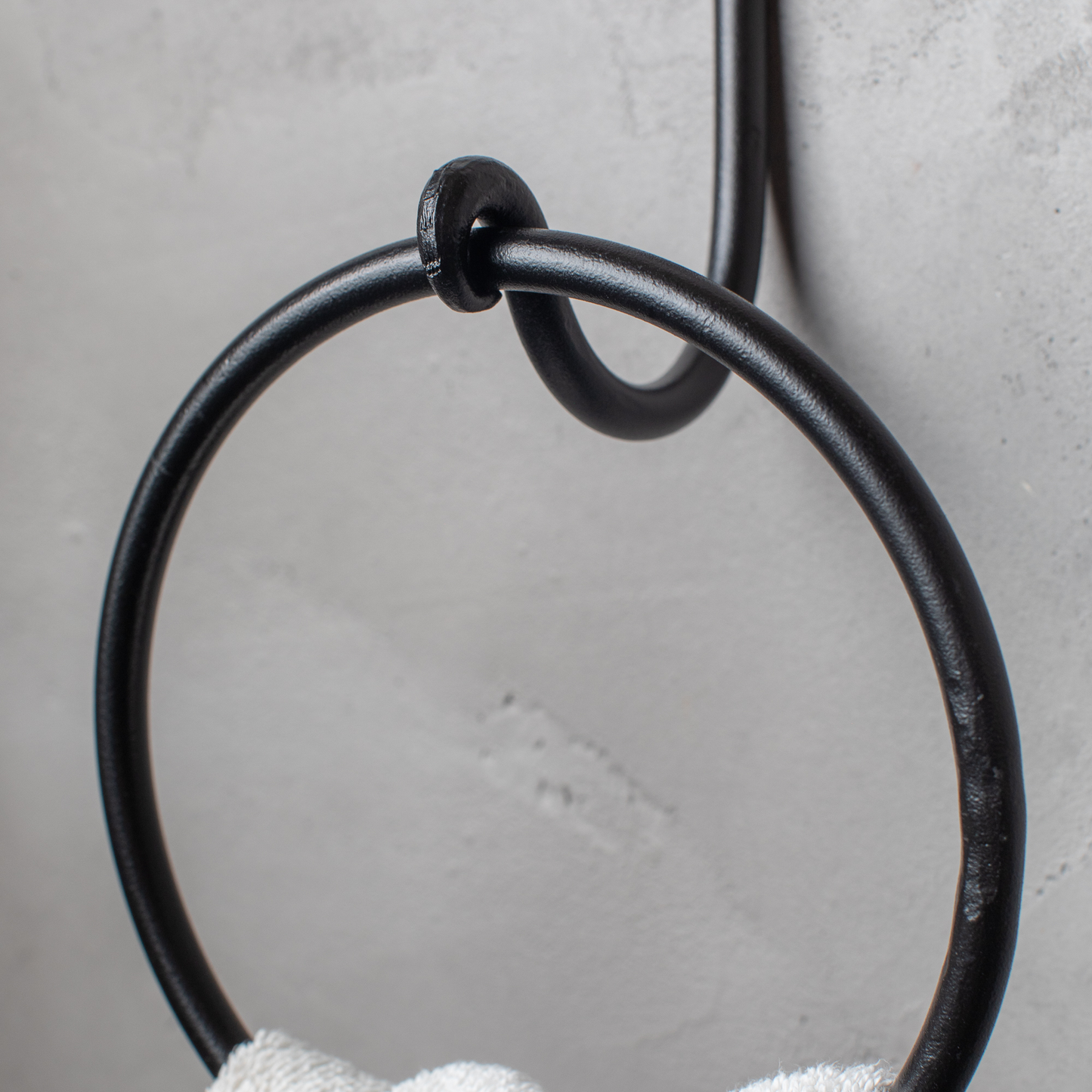 The Urban Forge Knot towel ring in a black finish. The towel ring is mounted on a gray wall and is holding a towel.