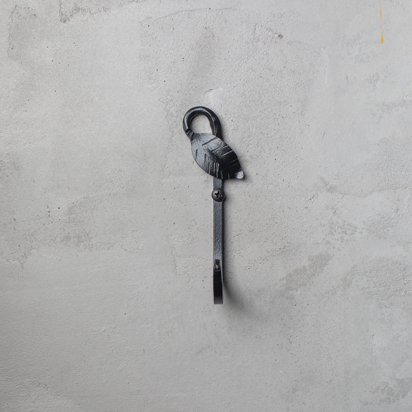 An Urban Forge Leaf hand-forged iron single hook in a black finish. The hook is mounted on a gray wall.