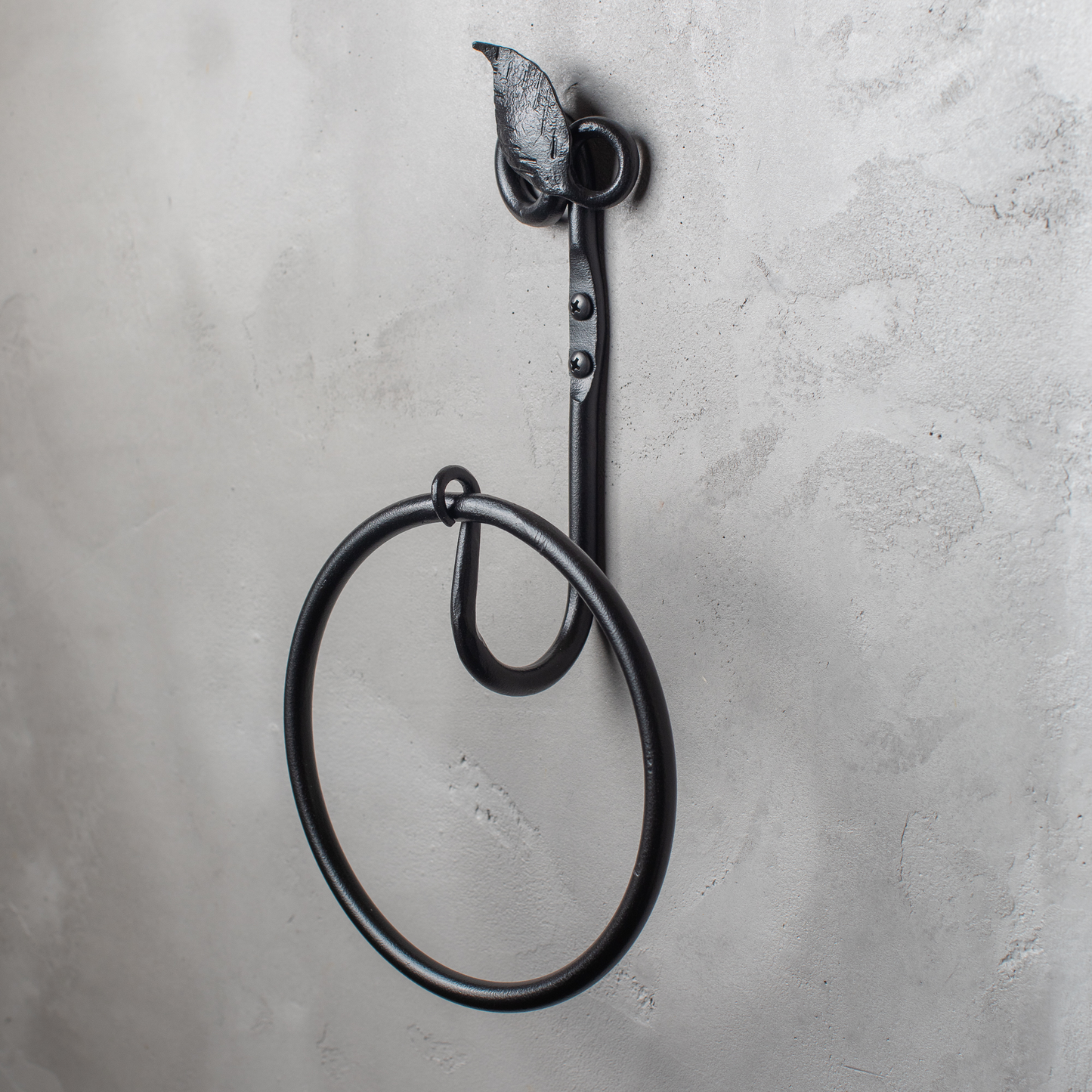 The Urban Forge Leaf towel ring in a black finish. The towel ring is mounted on a gray wall.