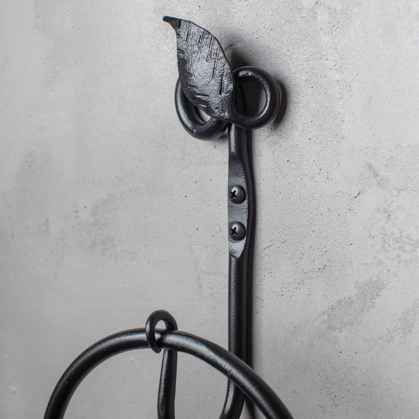 The Urban Forge Leaf towel ring in a black finish. The towel ring is mounted on a gray wall.