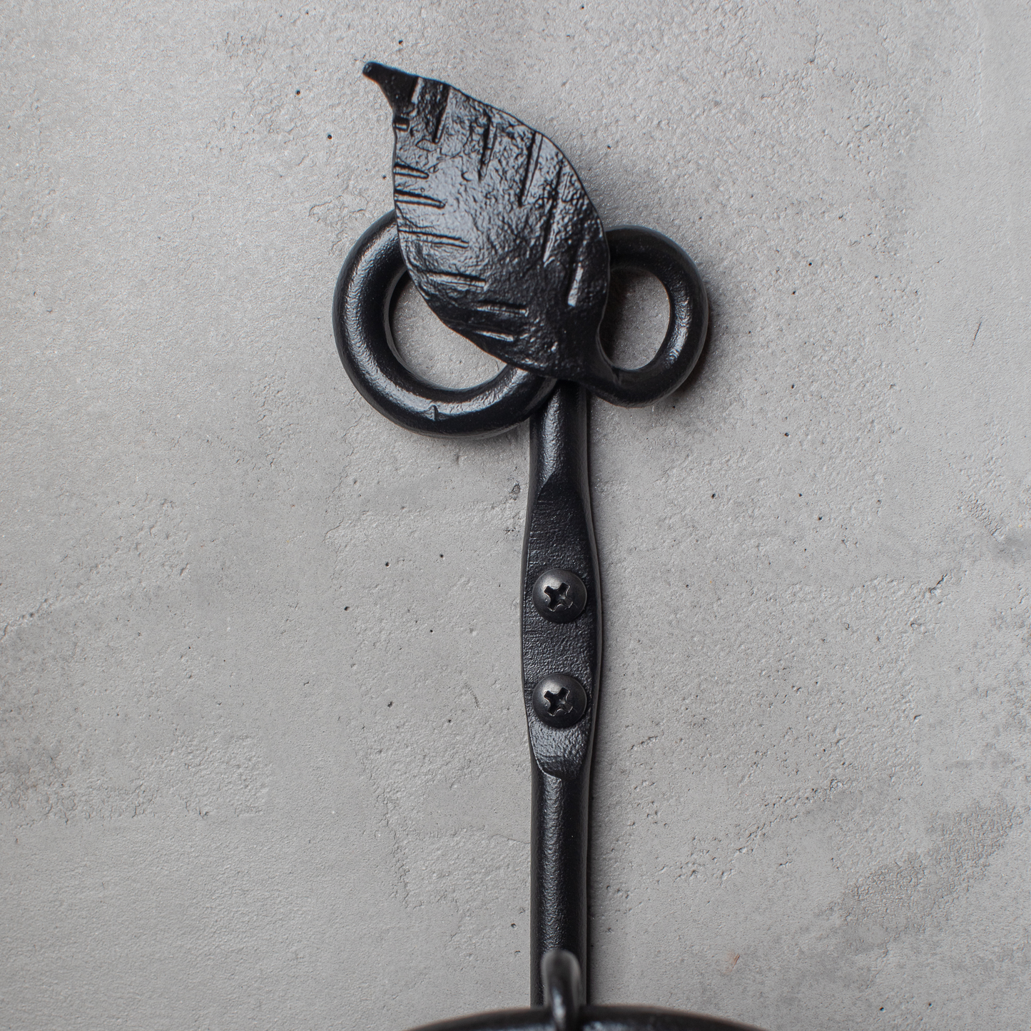 The Urban Forge Leaf towel ring in a black finish. The towel ring is mounted on a gray wall.