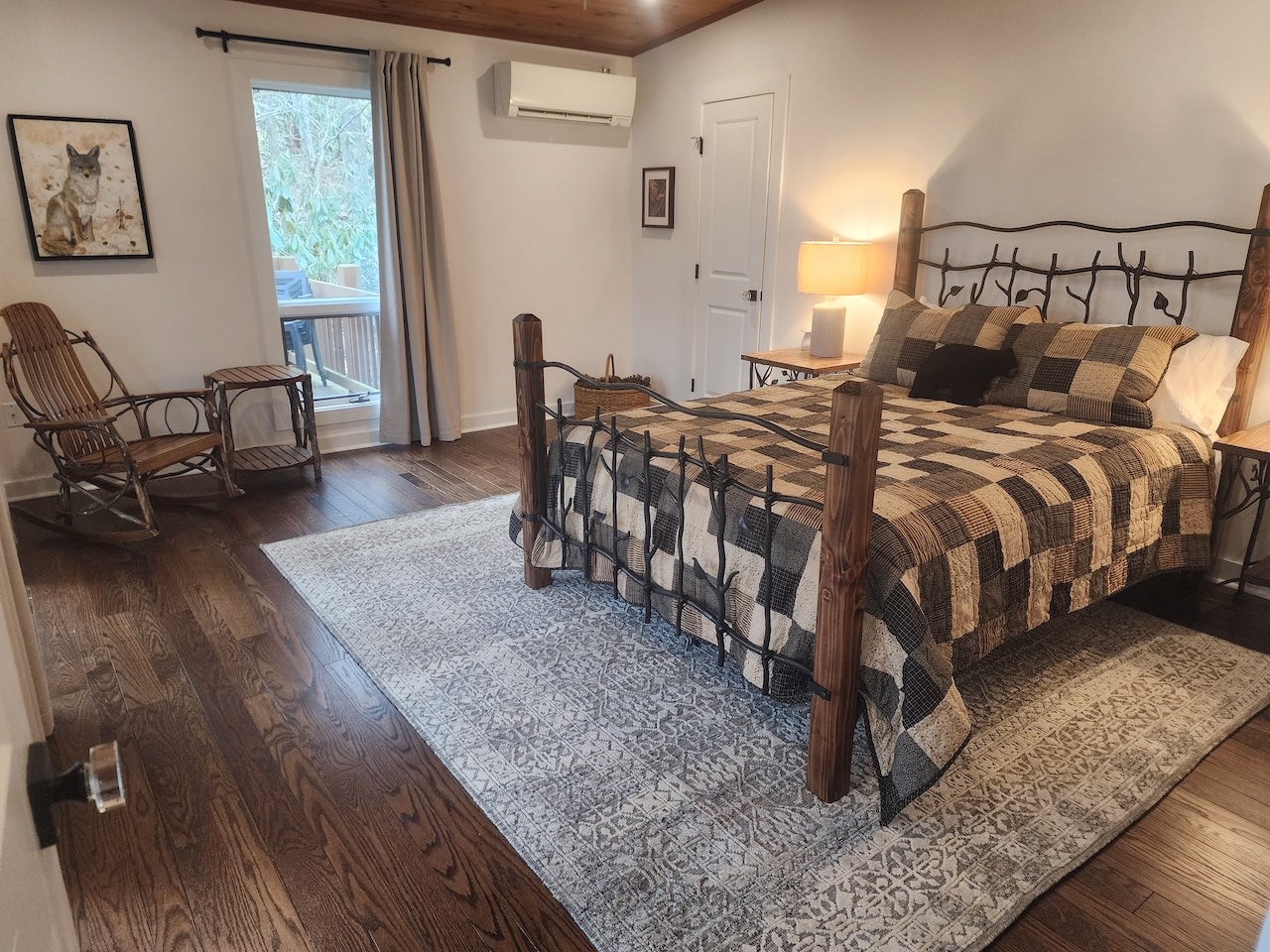 Bedroom with wooden and iron bed, rocking chair, and air conditioner.