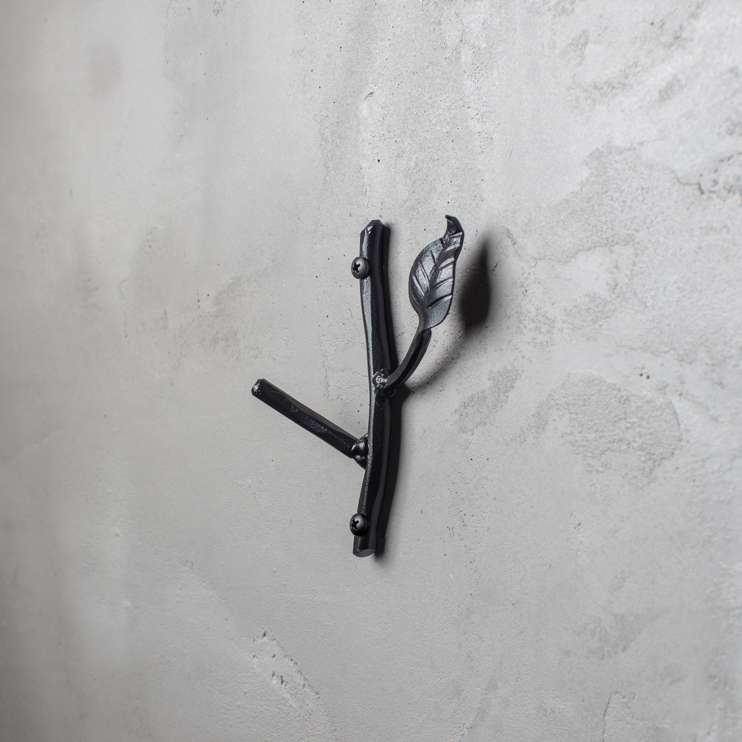 An Urban Forge Sylamore hand-forged iron single hook in a black finish. The hook is mounted on a gray wall.