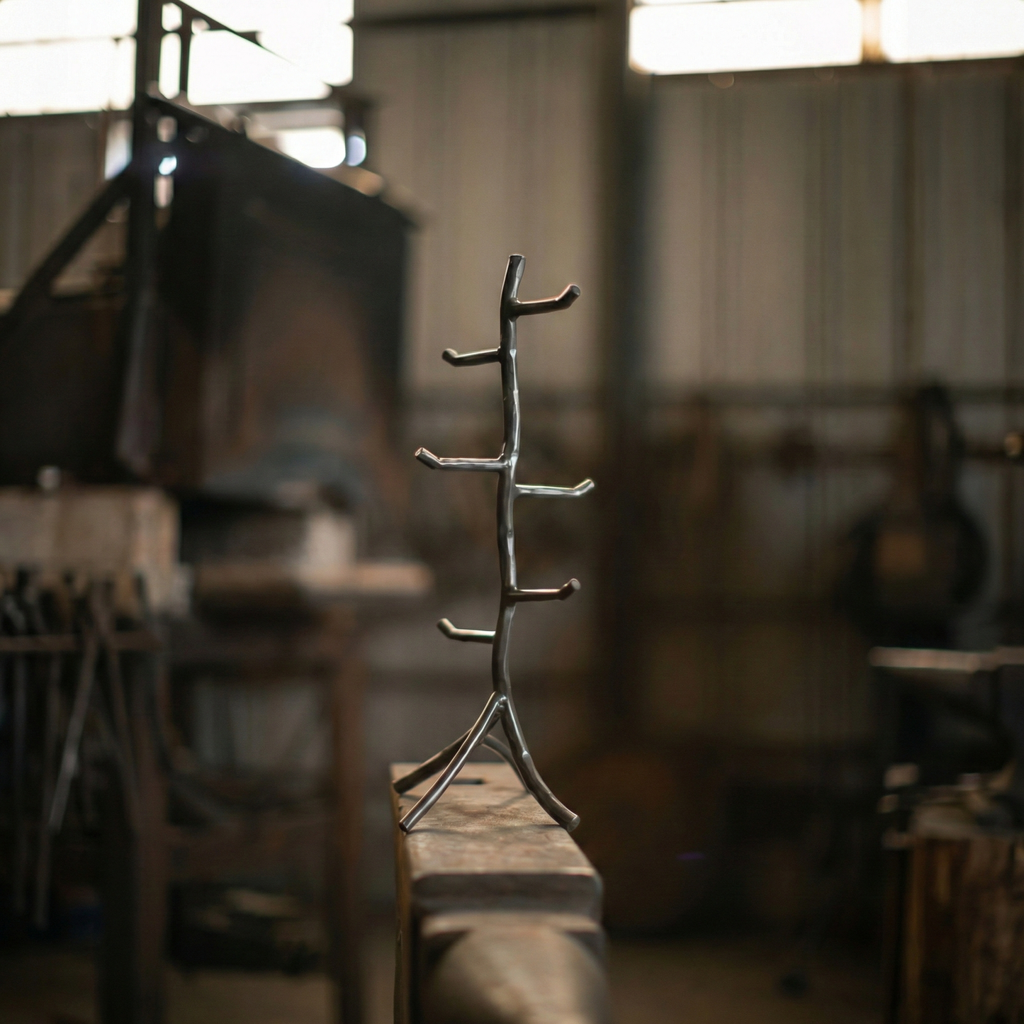 A hand-forged iron mug tree sitting on an anvil in a blacksmith forge.