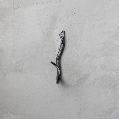 An Urban Forge Black River hand-forged iron single hook in a black finish. The hook is mounted on a gray wall.