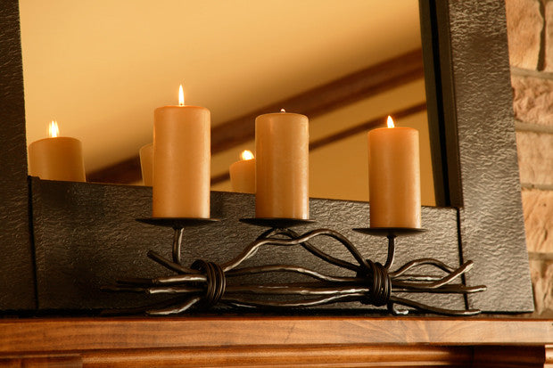 The Urban Forge Black River triple candle holder in a black finish. The candle holder has three amber candles and is resting on a fireplace.
