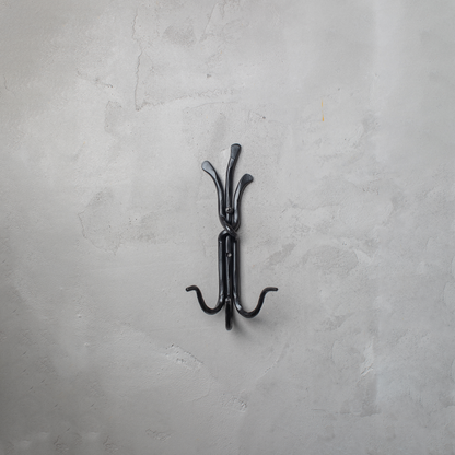An Urban Forge Black River hand-forged iron triple hook in a black finish. The hook is mounted on a gray wall.