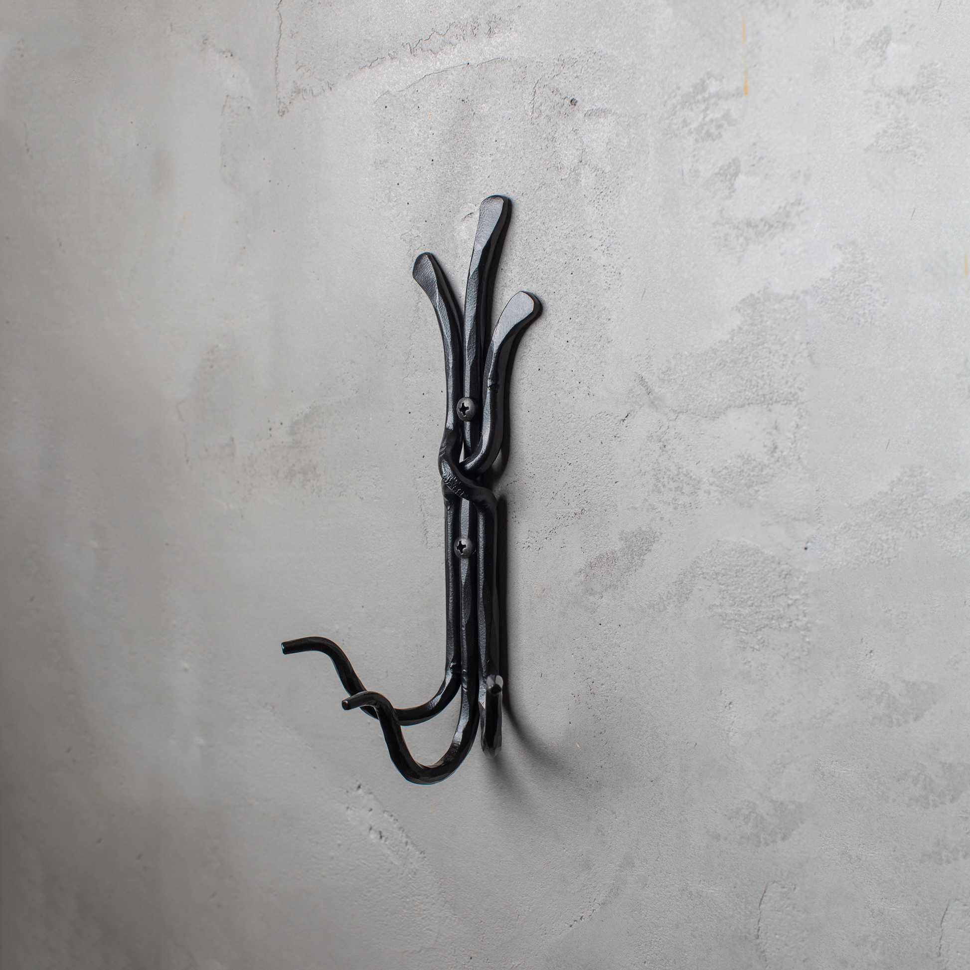 An Urban Forge Black River hand-forged iron triple hook in a black finish. The hook is mounted on a gray wall.