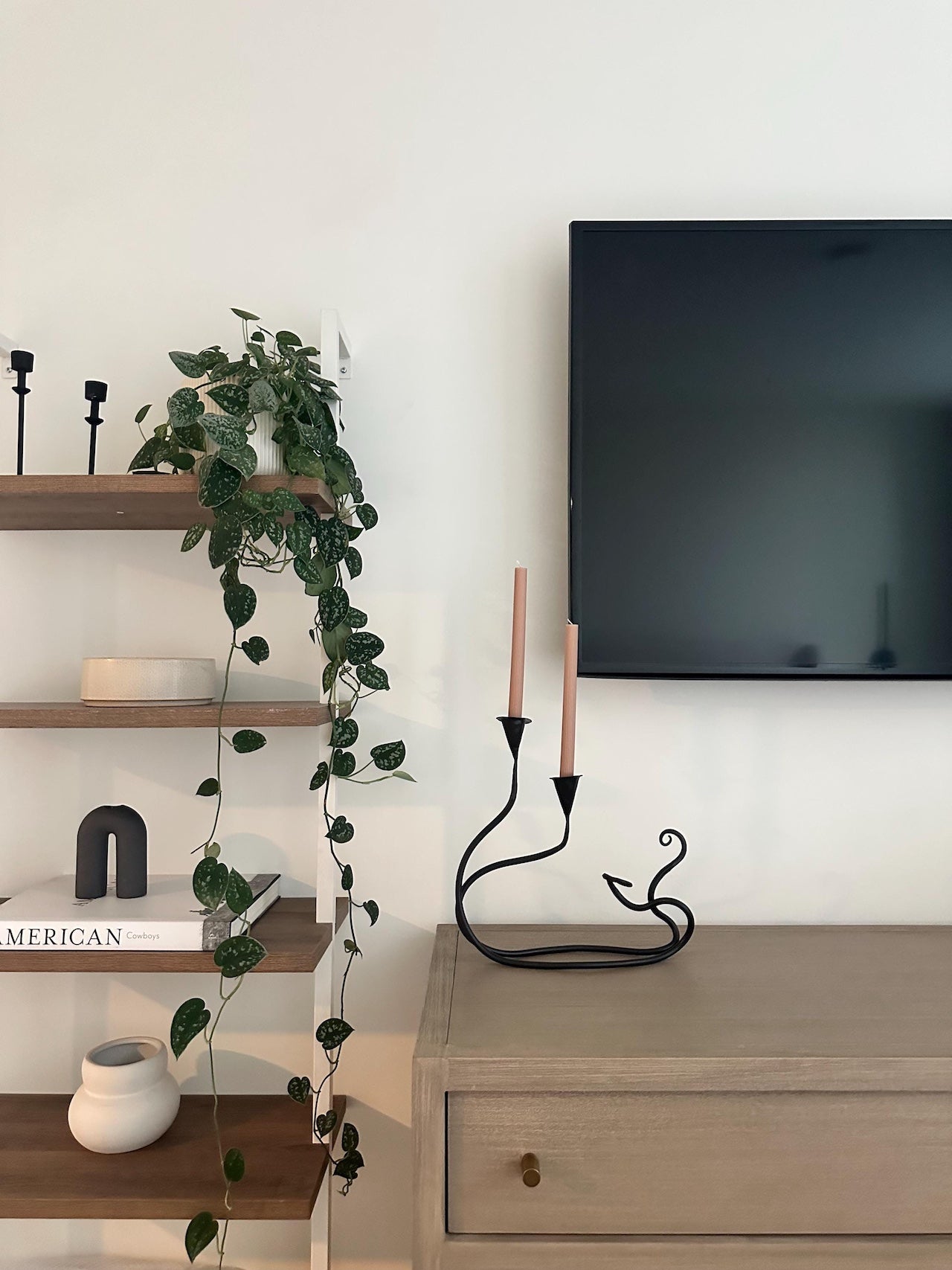 An Urban Forge Ivy double candle holder resting on an entertainment center next to a bookshelf.