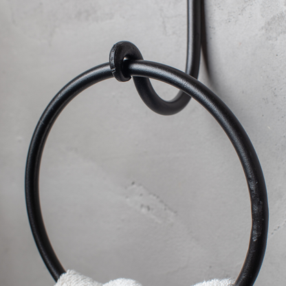 The Urban Forge Knot towel ring in a black finish. The towel ring is mounted on a gray wall and is holding a towel.