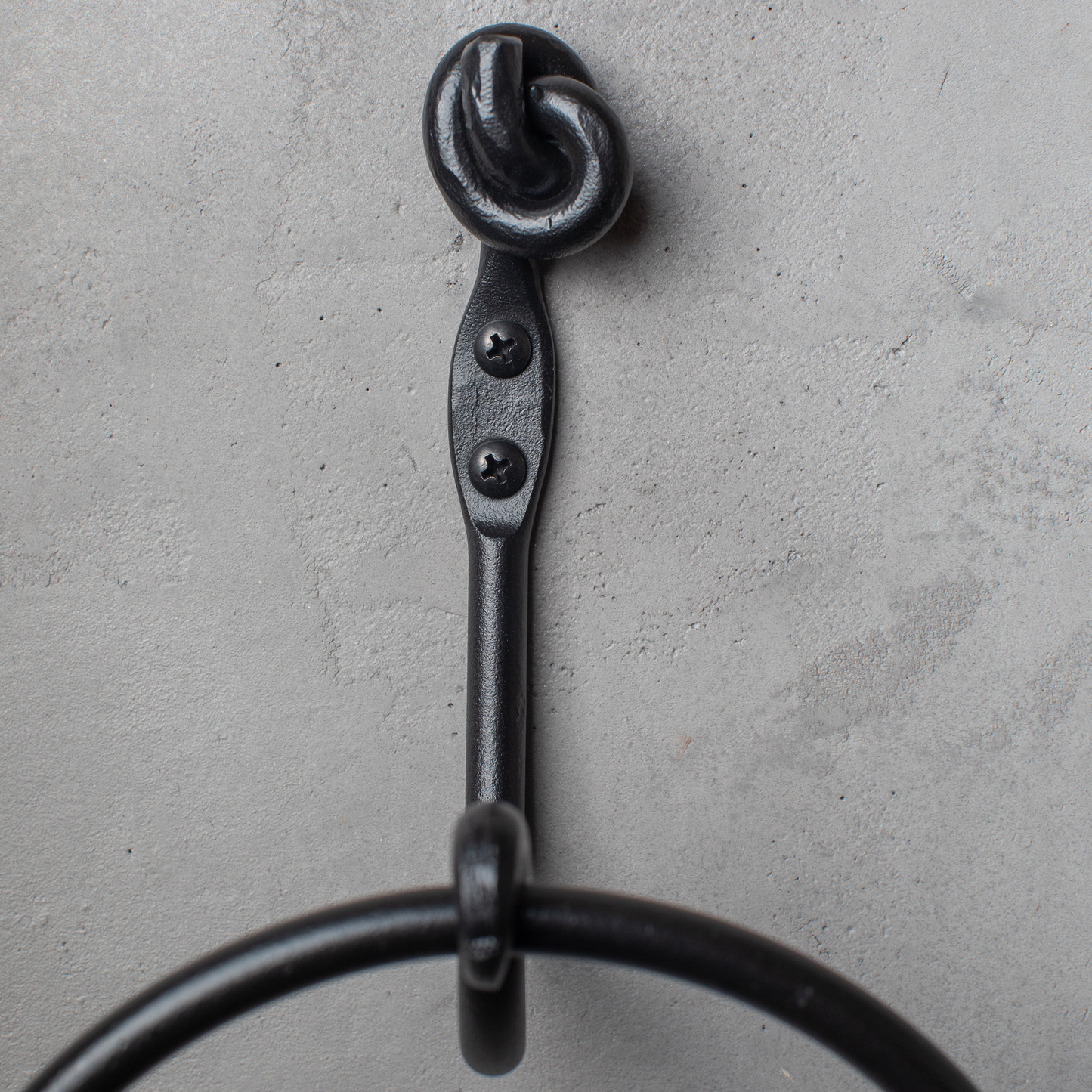 The Urban Forge Knot towel ring in a black finish. The towel ring is mounted on a gray wall.