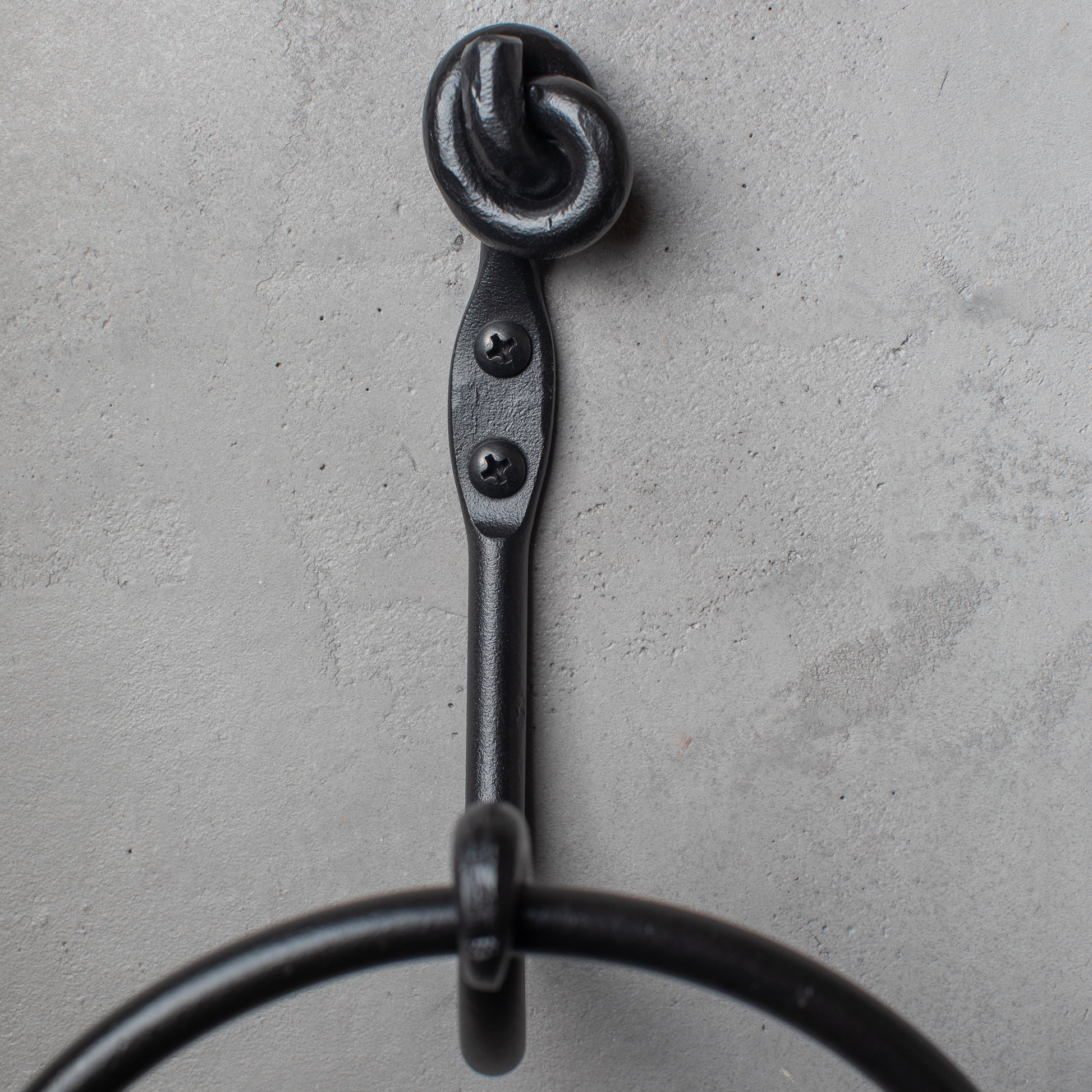 The Urban Forge Knot towel ring in a black finish. The towel ring is mounted on a gray wall.