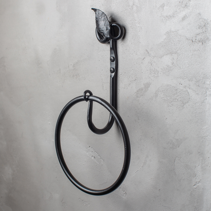 The Urban Forge Leaf towel ring in a black finish. The towel ring is mounted on a gray wall.