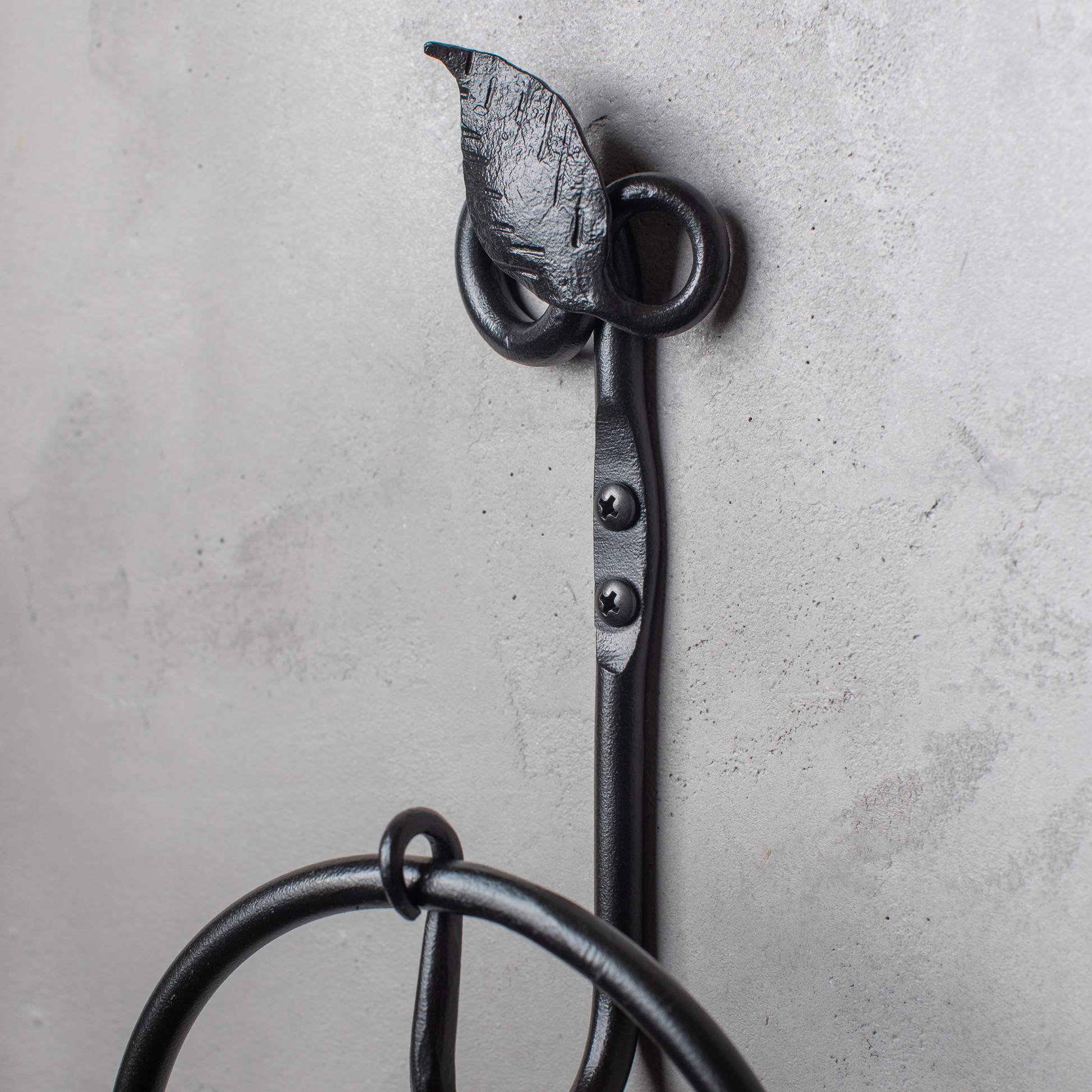The Urban Forge Leaf towel ring in a black finish. The towel ring is mounted on a gray wall.