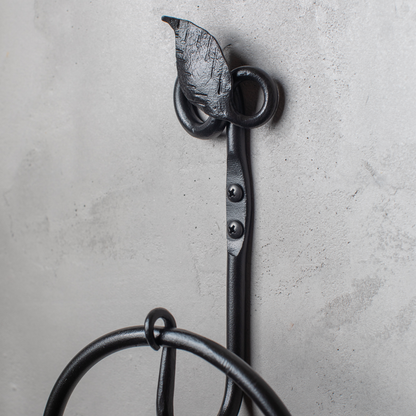 The Urban Forge Leaf towel ring in a black finish. The towel ring is mounted on a gray wall.