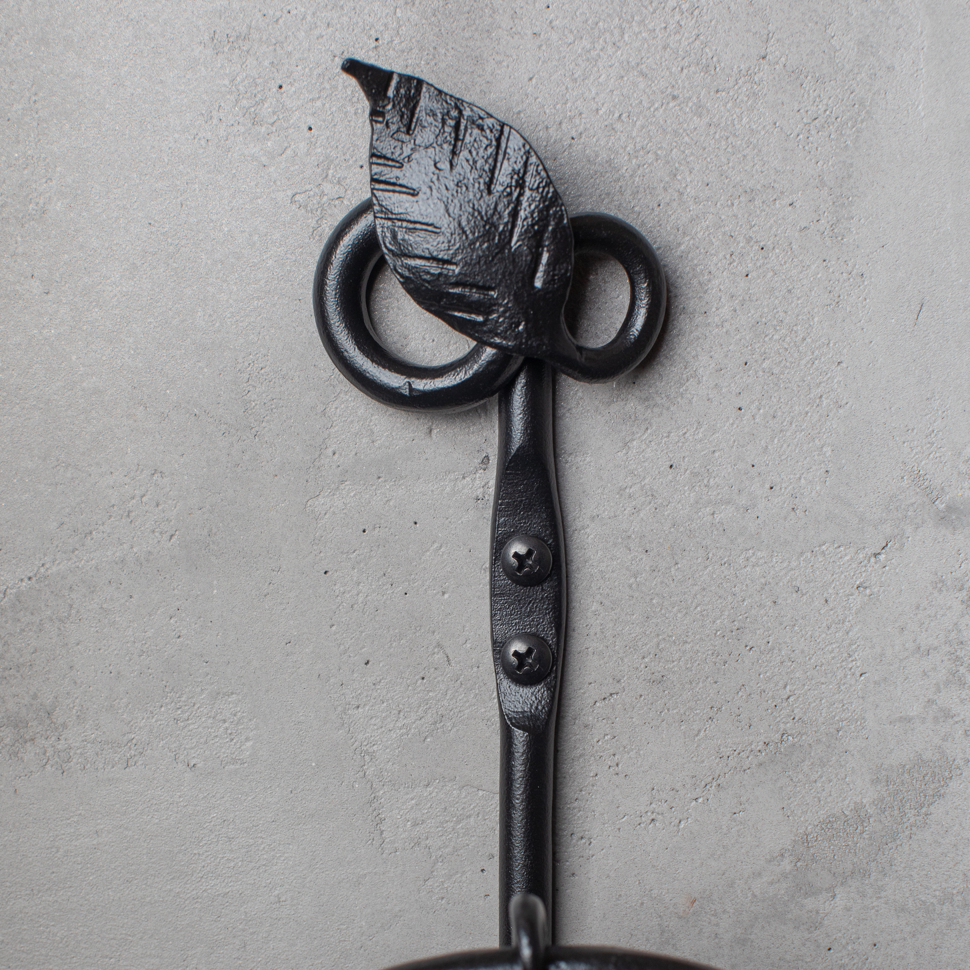 The Urban Forge Leaf towel ring in a black finish. The towel ring is mounted on a gray wall.