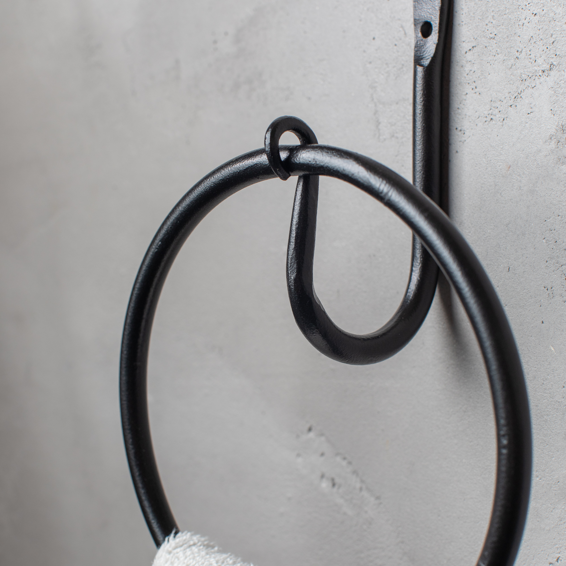 The Urban Forge Leaf towel ring in a black finish. The towel ring is mounted on a gray wall and is holding a towel.