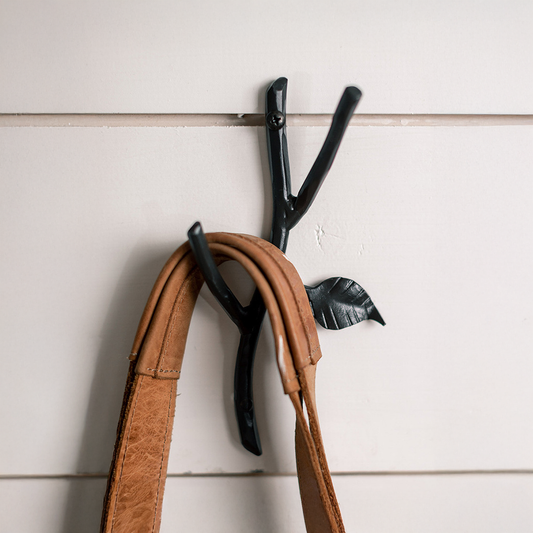 An Urban Forge Sylamore hand-forged iron double hook in a black finish. The hook is mounted on a white shiplap wall.