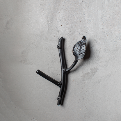 An Urban Forge Sylamore hand-forged iron single hook in a black finish. The hook is mounted on a gray wall.