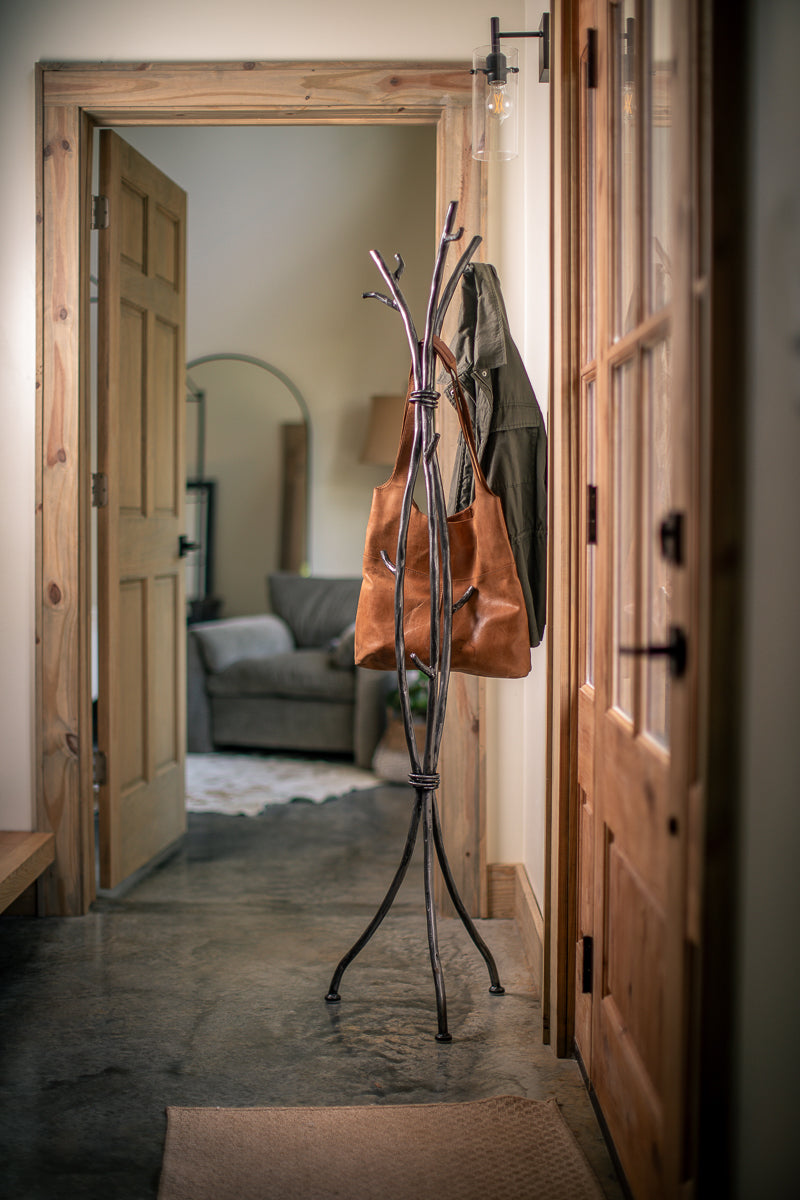 An Urban Forge Sylamore iron standing coat rack in a silver finish. The coat rack is holding a leather bag.