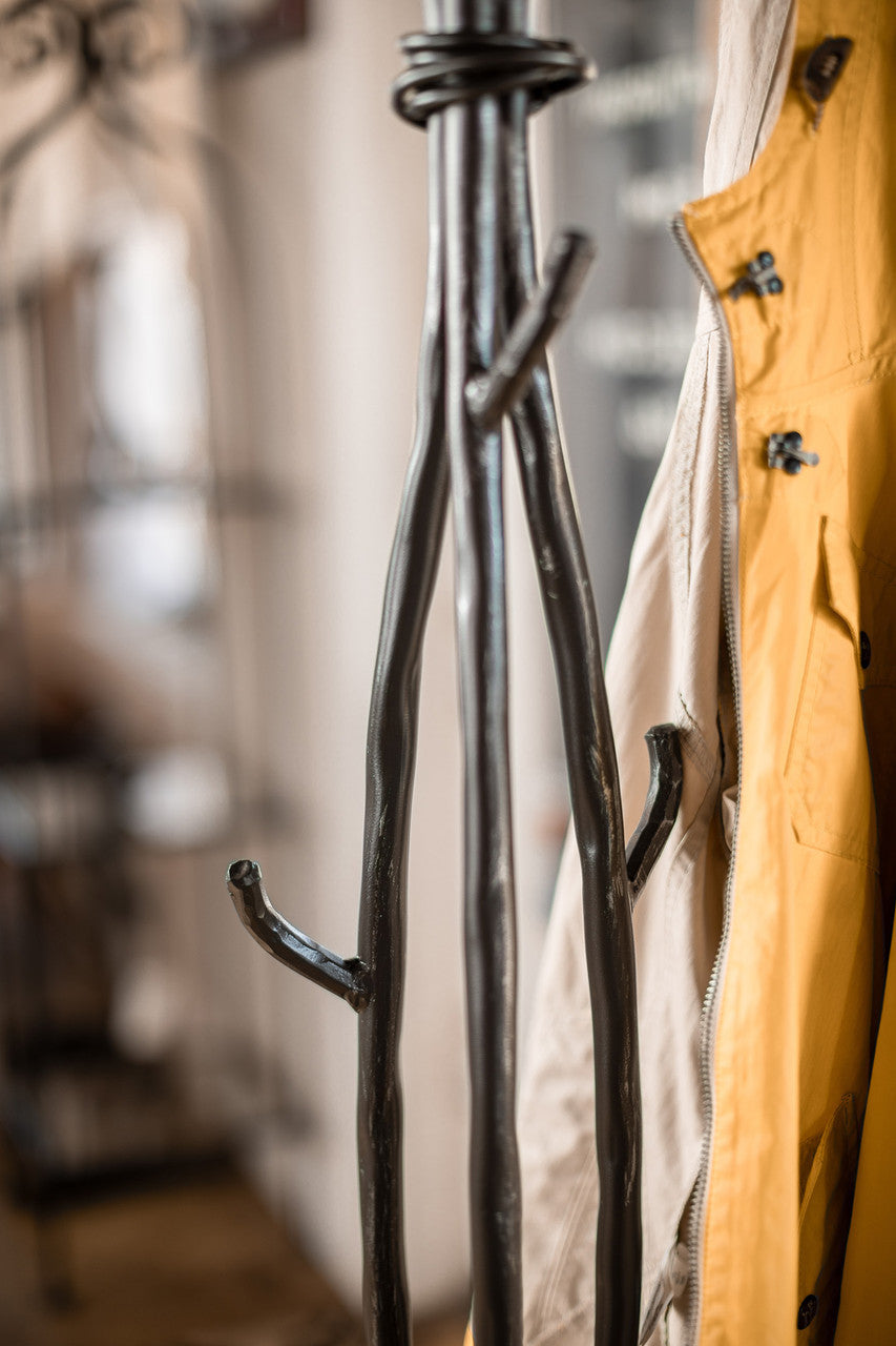 An Urban Forge Sylamore iron standing coat rack in a black finish. The coat rack is holding a yellow jacket.