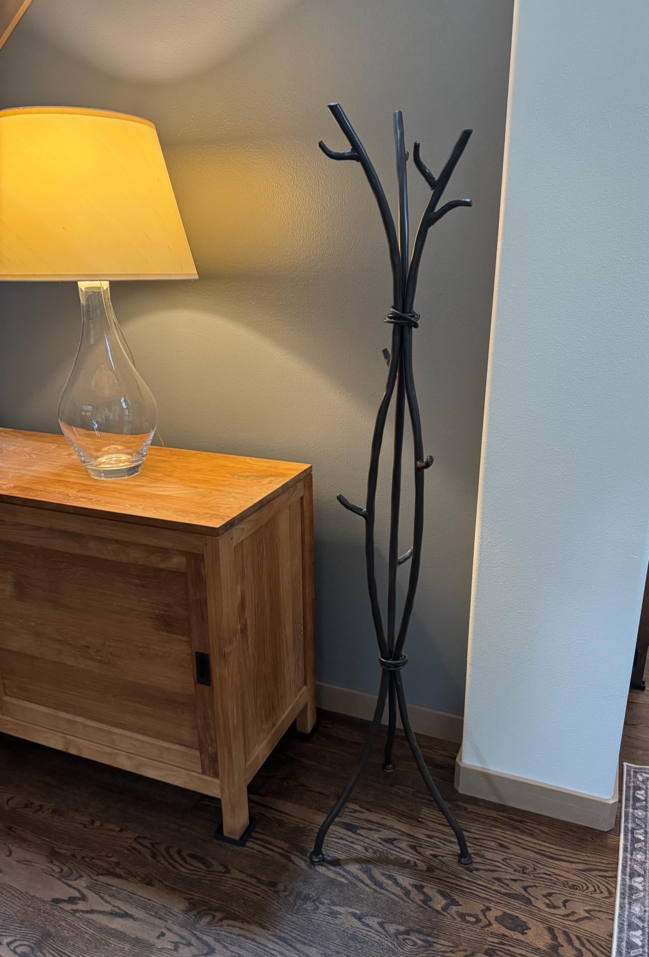 Wooden side table with lamp and black twig-style coat rack against a wall.