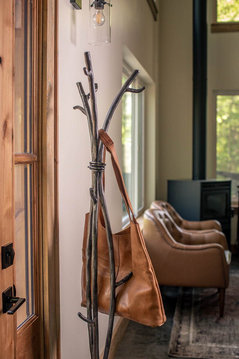 An Urban Forge Sylamore iron standing coat rack in a silverfinish. The coat rack is holding a leather bag.